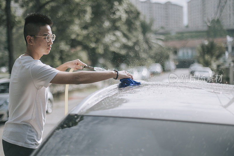 an asian chinese teenager boy washing and cleaning car in front of his house